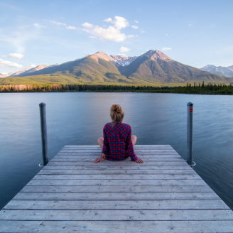 A person sitting at the end of a deck looking out at a senic body of water and mountains