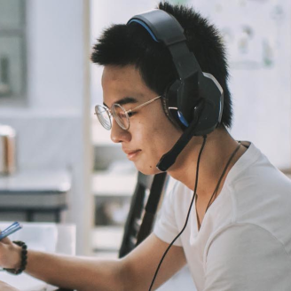 Une personne d’origine asiatique portant des écouteurs travaille sur son ordinateur portable