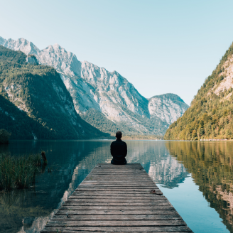 Une personne assise au bout d’un quai regarde vers un plan d’eau et des montagnes