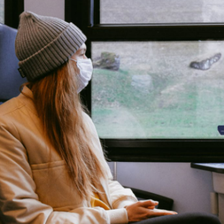 Une personne portant un masque qui regarde par la fenêtre d’un train