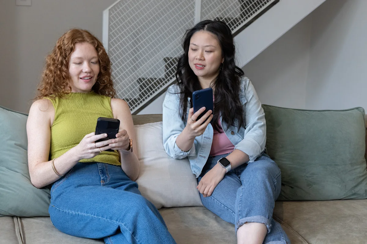 two women sitting with their phones on a sofa