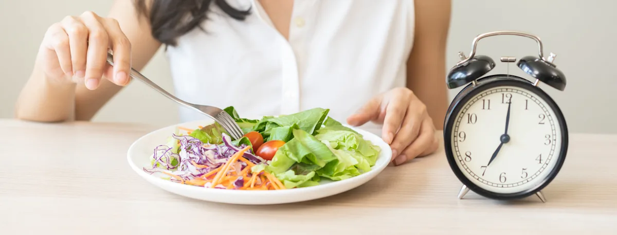 woman in front of a plate of salad and an alarm clock