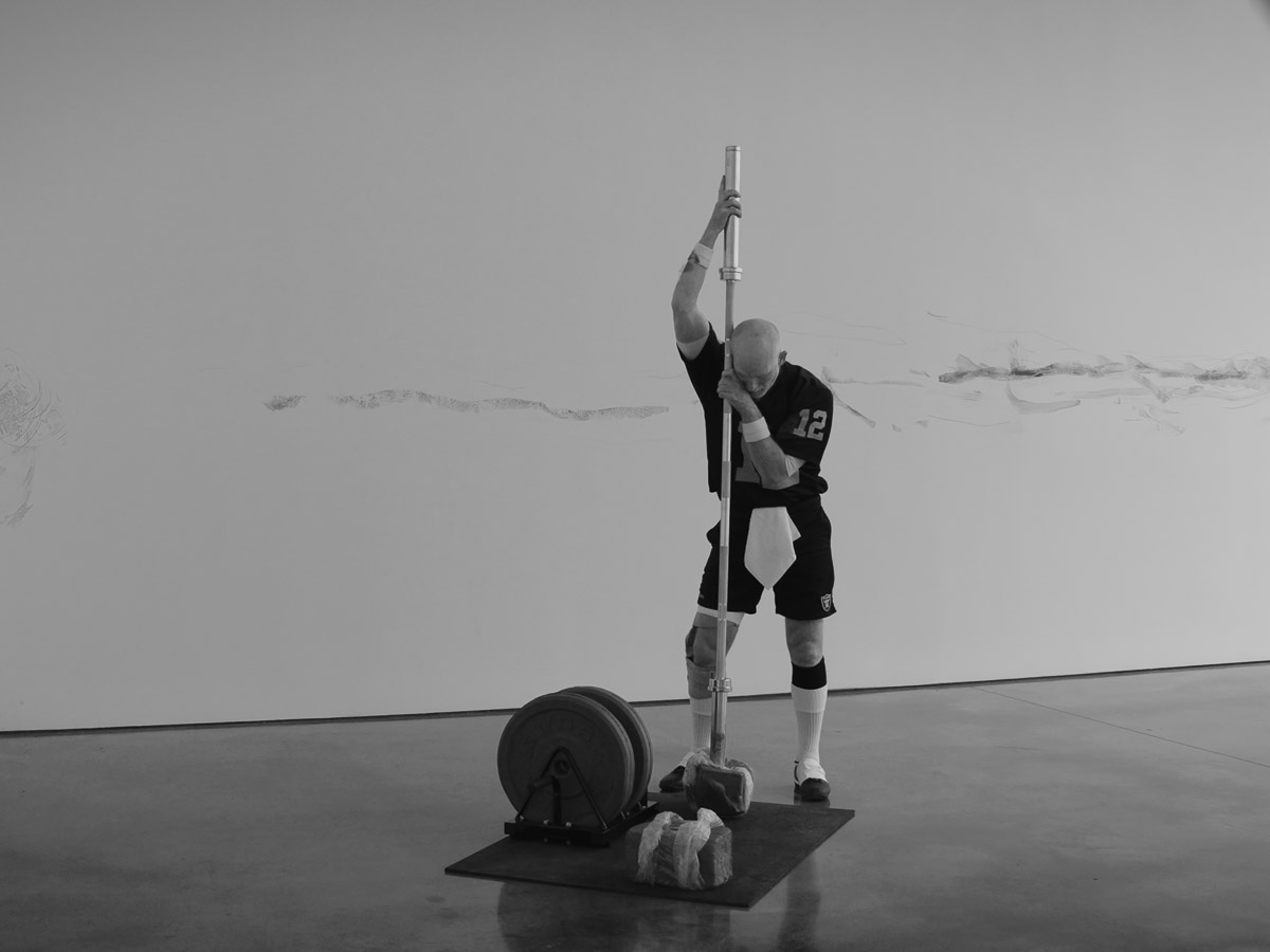 Black and white image of a man wearing a football jersey performing choreography in a white room with a concrete floor