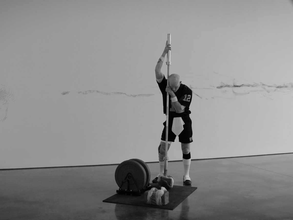 Black and white image of a man wearing a football jersey performing choreography in a white room with a concrete floor