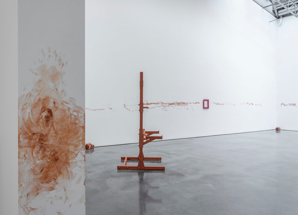 Art exhibition installation with pigment and framed art on the walls of the room and sculptures on the floor.