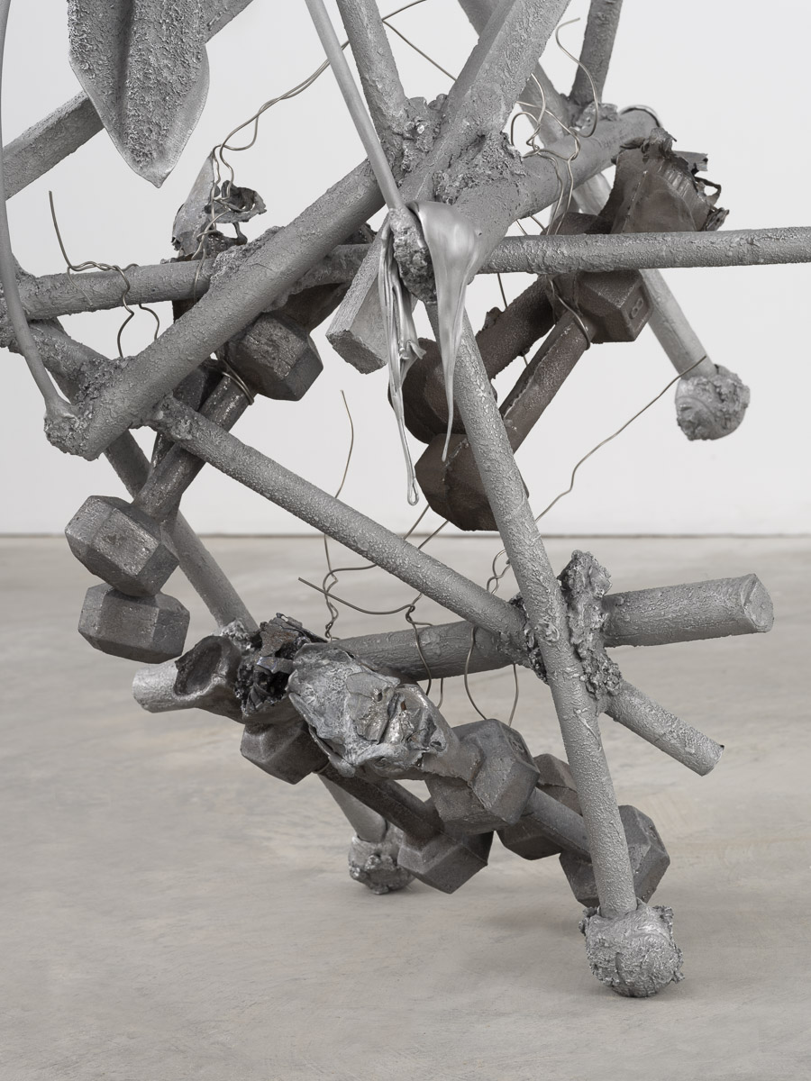 Detail view of an aluminum and lead sculpture in a white room on a concrete floor. 