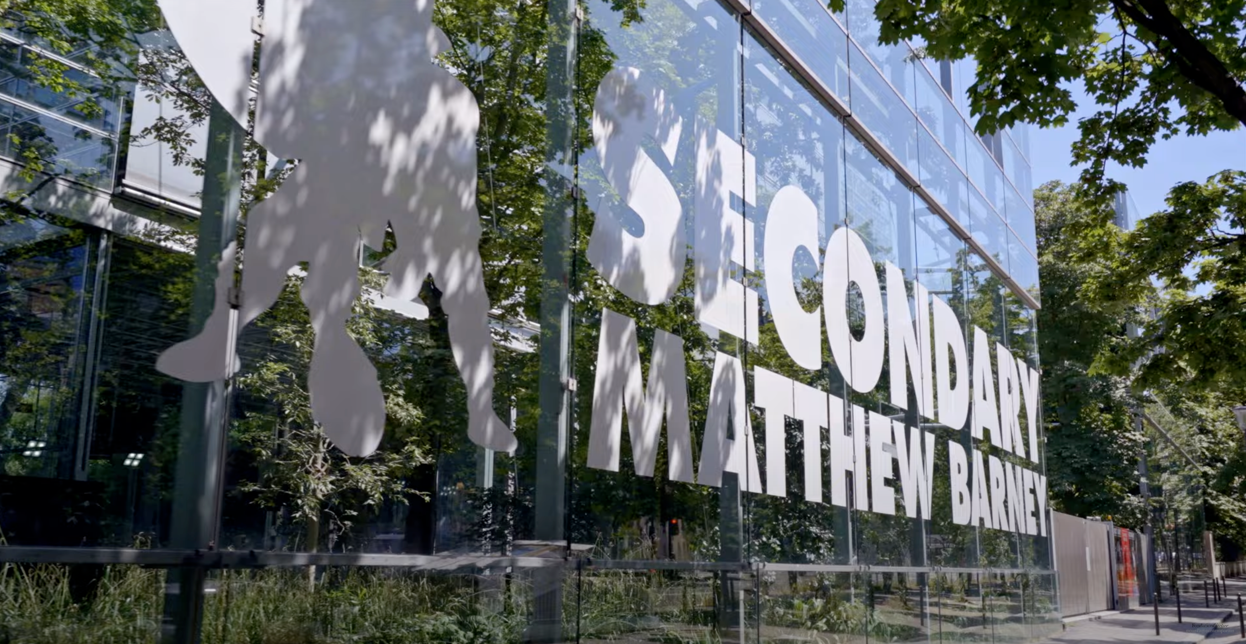 Glass facade with white signage reading SECONDARY, MATTHEW BARNEY