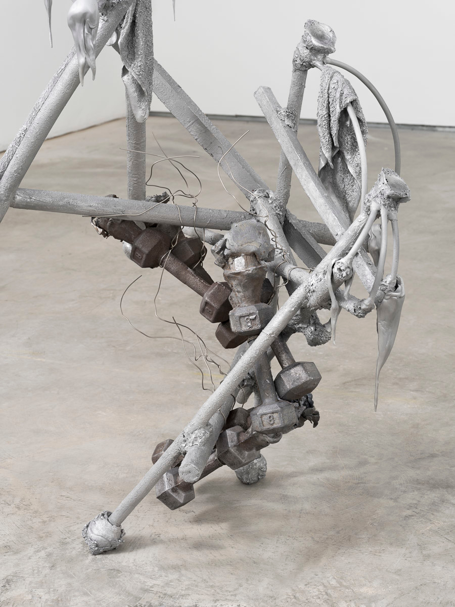 Detail view of an aluminum and lead sculpture in a white room on a concrete floor.