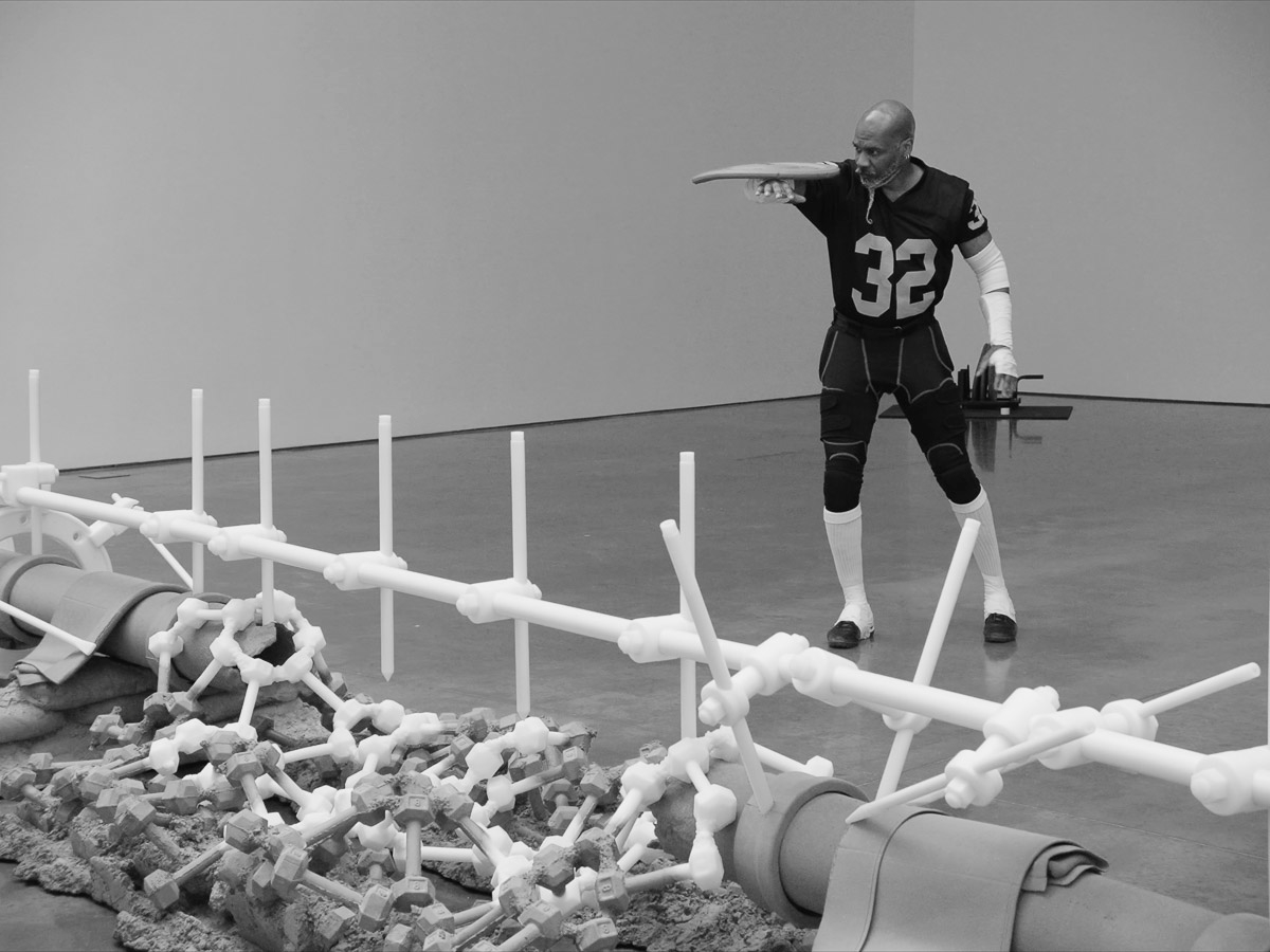 black and white video still image of a man wearing a jersey numbered 32 with a sculpture partially in view