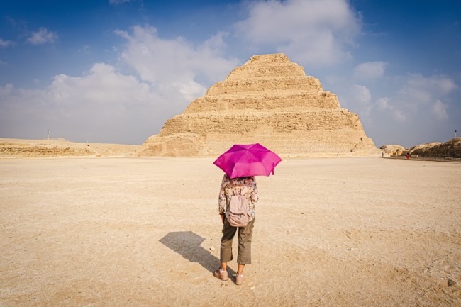View of a woman with a purple umbrella watching the scale pyramid of Djoser in the Saqqara necropolis. 