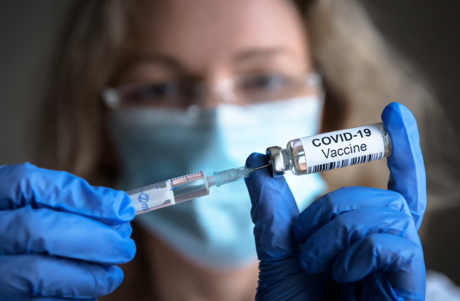 female medical professional wearing a mask and gloves holding a COVID-19-vaccine