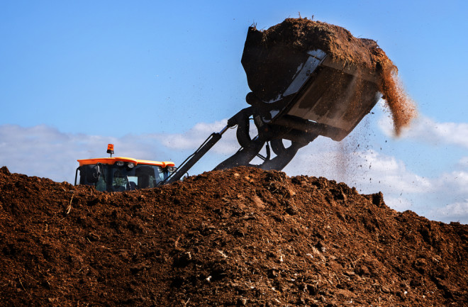 Excavator shovel working on a large heap of manure, organic fertilizer for the field, blue sky - shutterstock 469583543