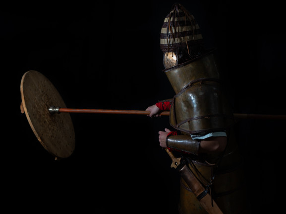 Participant wearing armor and hitting a shield while holding a spear.
