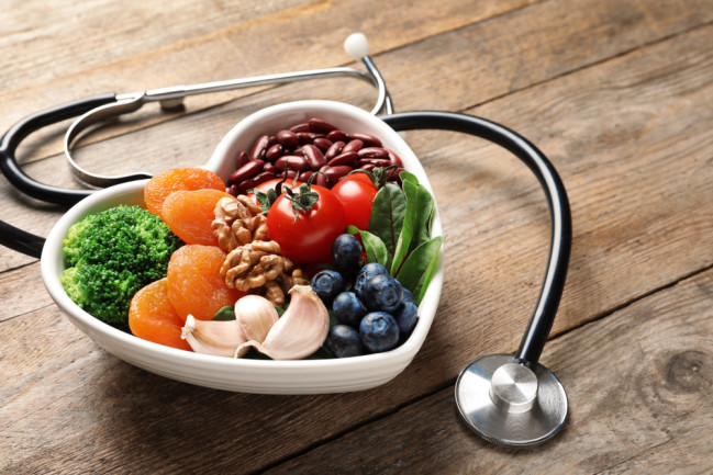 Bowl with heart-healthy diet products and stethoscope on wooden table. Space for text