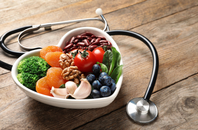 Bowl with heart-healthy diet products and stethoscope on wooden table. Space for text