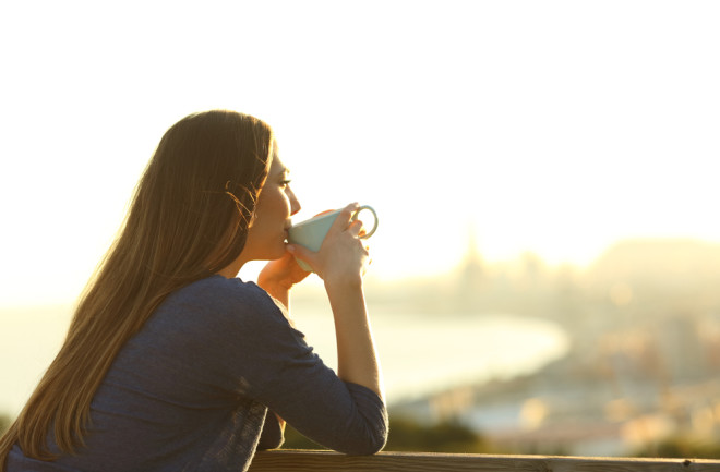 Woman drinking coffee on balcony, sunrise sunset - Shutterstock