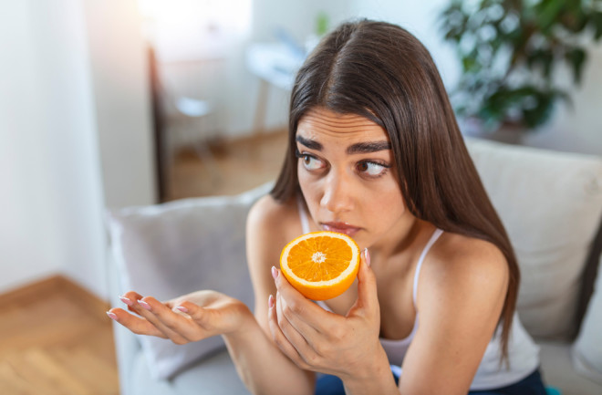 Sick woman trying to smell half of a fresh orange