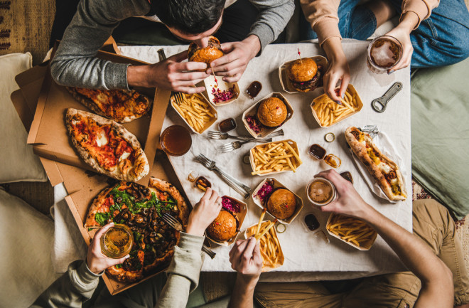 Friends sitting and having a party. Overeating with an abundance of food, burgers, french fries, sandwiches, pizza, salad