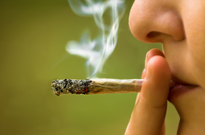 woman smoking a marijuana joint against a green background - shutterstock 157734158