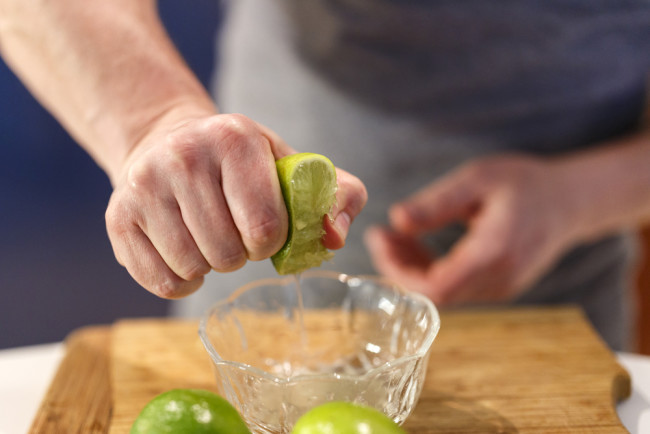 Hands squeezing a lime into a bowl - Shutterstock