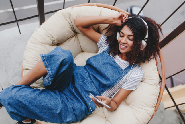 young woman in vintage denim clothes chilling on terrace in white headphones.
