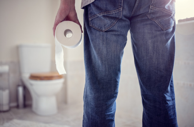 man facing toilet holding toilet paper in bathroom - shutterstock 644195584