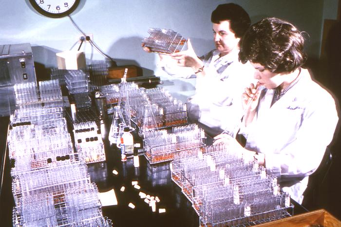 Former Centers for Disease Control (CDC) parasitologist, Dr. Mae Melvin (Lt), examines a collection of test tubes while her laboratory assistant mouth pipettes a culture to be added to these test tubes. Source: David Senser/CDC.
