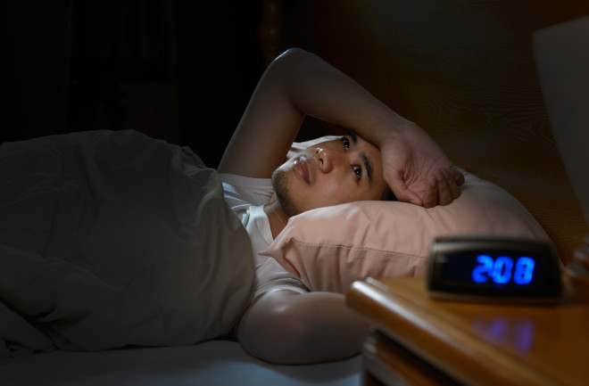 Man in bed awake at night insomnia - shutterstock