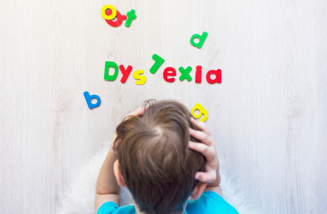 A school aged boy holding his head in hands in frustration because of dyslexia failing to read magnetic letters shot from above horizontal.