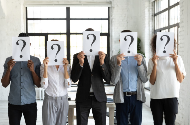 Diverse business people hiding faces behind papers sheets with question marks, standing in row in office.