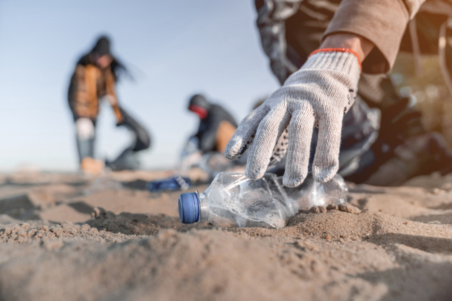 beach cleanup crew collecting plastic bottles - shutterstock 1521472085