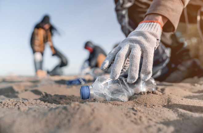 beach cleanup crew collecting plastic bottles - shutterstock 1521472085