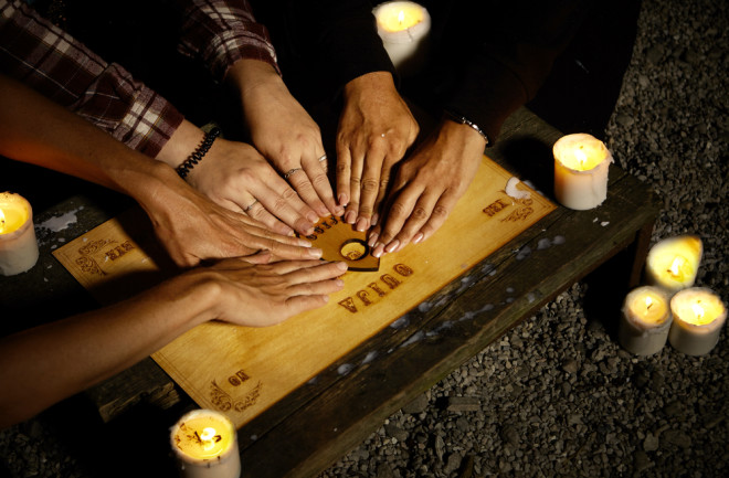 Three people conducting a seance using a Ouija Board with white candles. Shot from overhead.