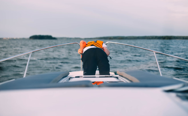 sea sick man on boat with orange life jacket throwing up over board