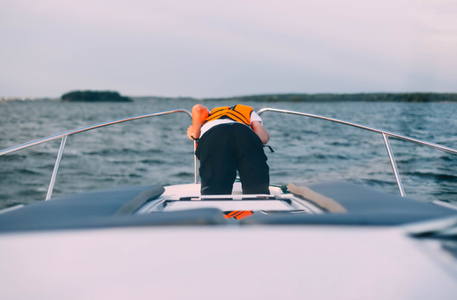 sea sick man on boat with orange life jacket throwing up over board
