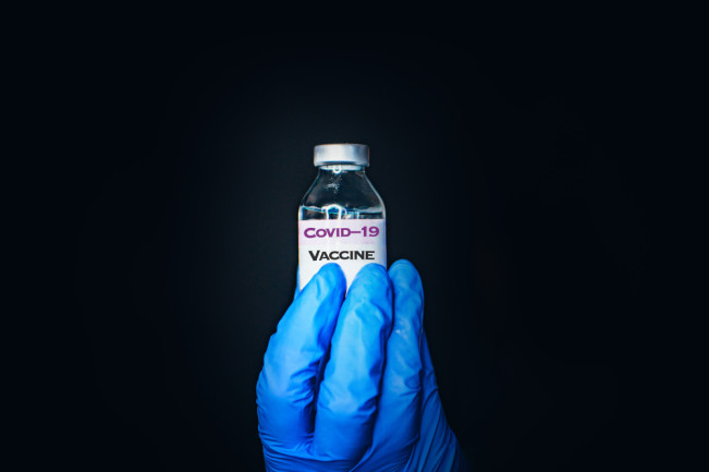 gloved hand holding a covid-19 vaccine vial - shutterstock