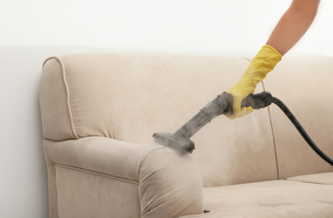 Arm with yellow rubber glove holds a hand-held steamer to a sofa - Shutterstock
