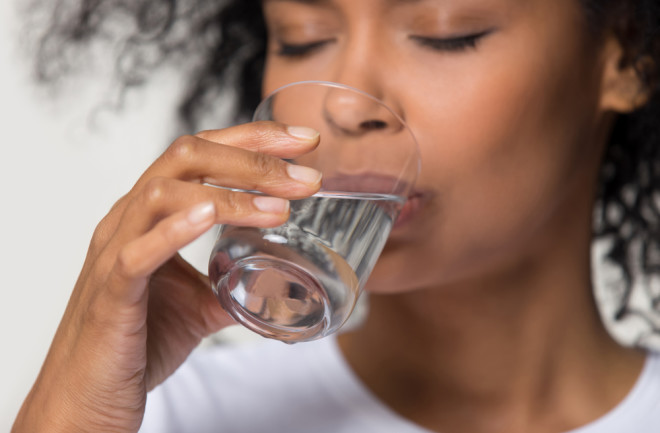 close up of woman drinking a glass of water - shutterstock 1391203490