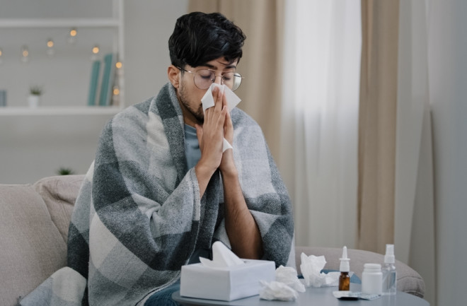 man on couch with a blanket blowing nose has a cold