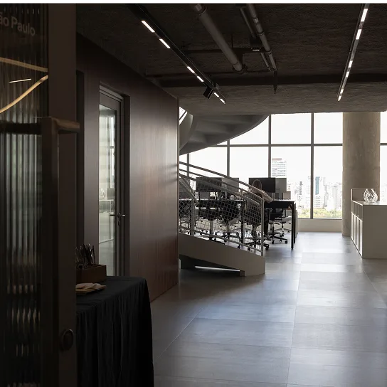 Modern office interior featuring a spiral staircase, workstations and chairs beside large floor-to-ceiling windows with a city view.