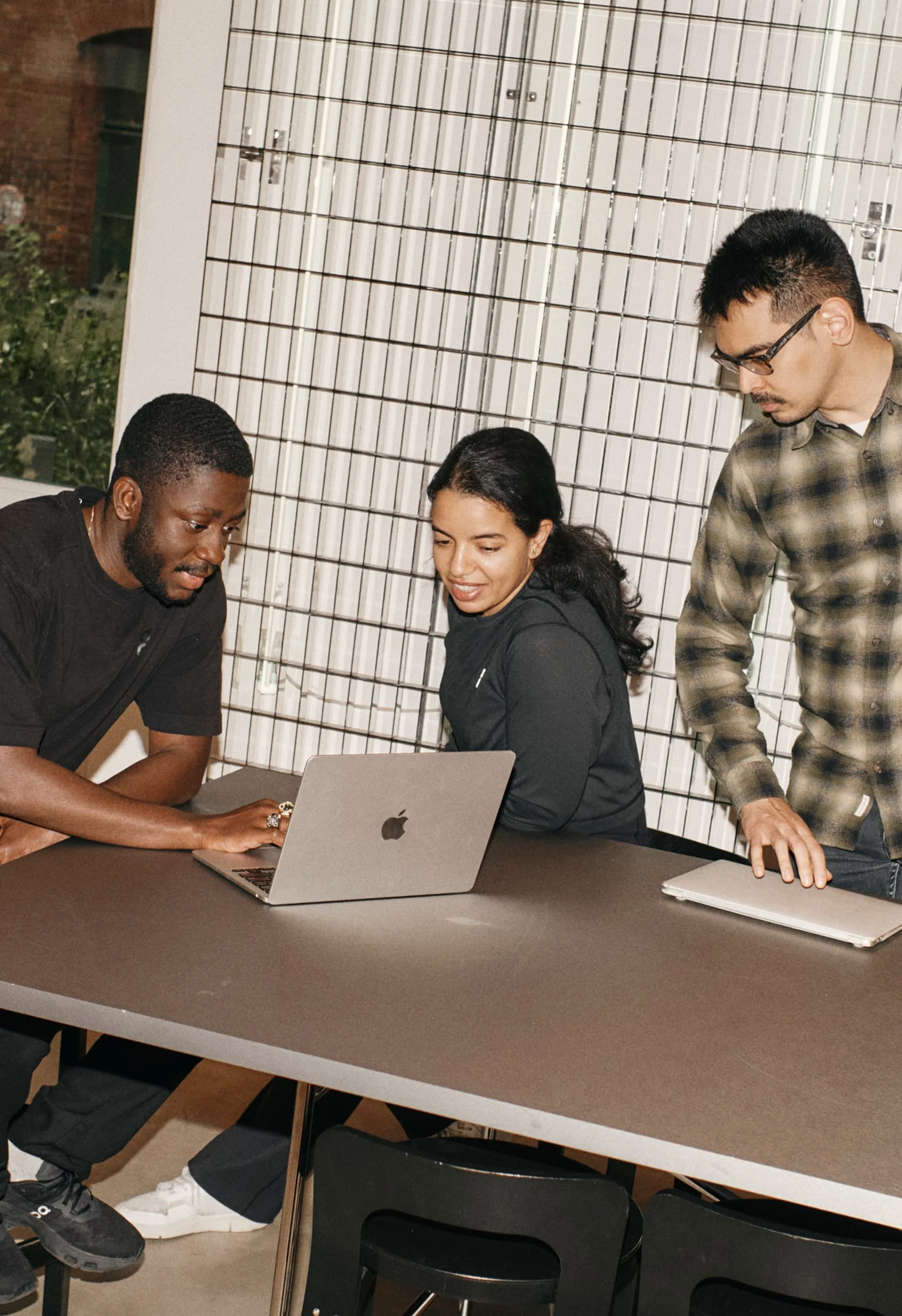 Three colleagues gather around a laptop, reviewing work together in a well-lit meeting space.
