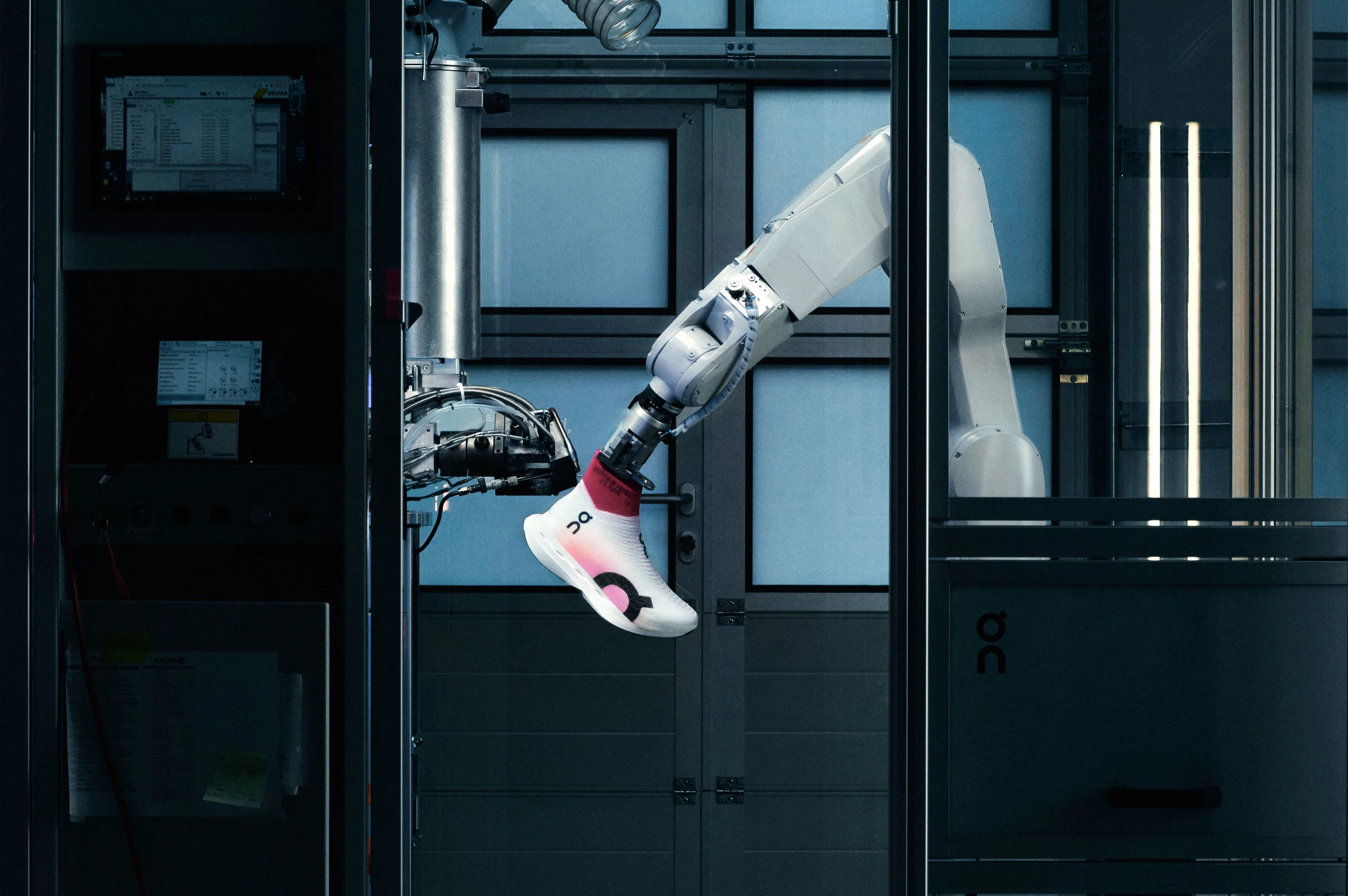 A shoe being held by a motorized robotic arm. It is being sprayed by a second machine with a knit-like webbing to create a lighweight upper material.