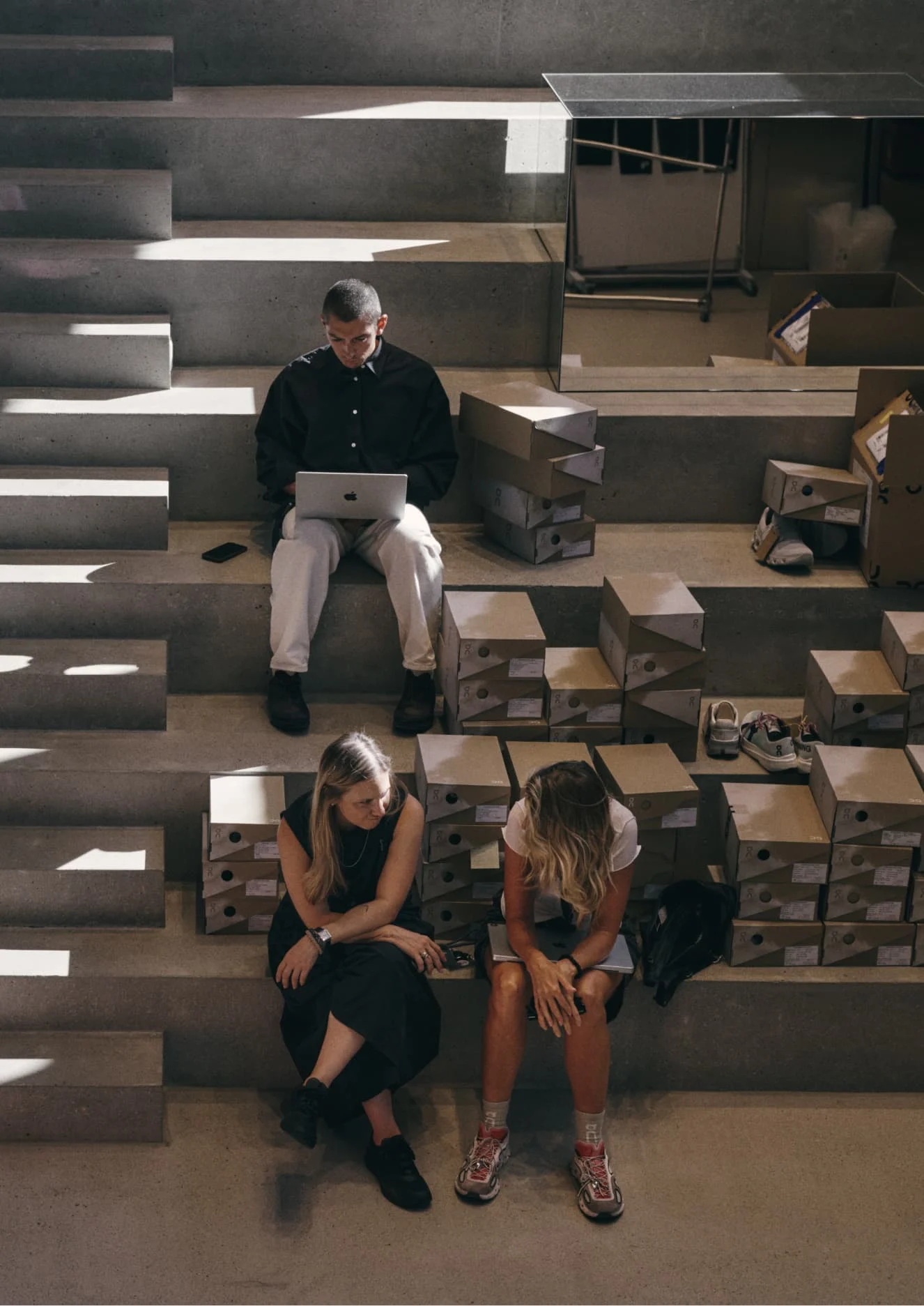 Three people work on a large concrete staircase surrounded by open cardboard shoe boxes and orange storage bins.
