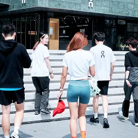 Five people in athletic clothing walk away from the camera toward steps leading into a modern building.