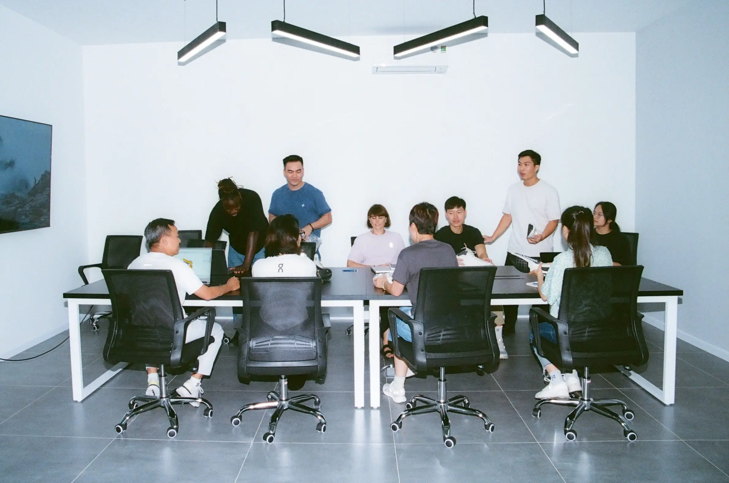 A diverse group of people seated and standing around a conference table in a bright meeting room.