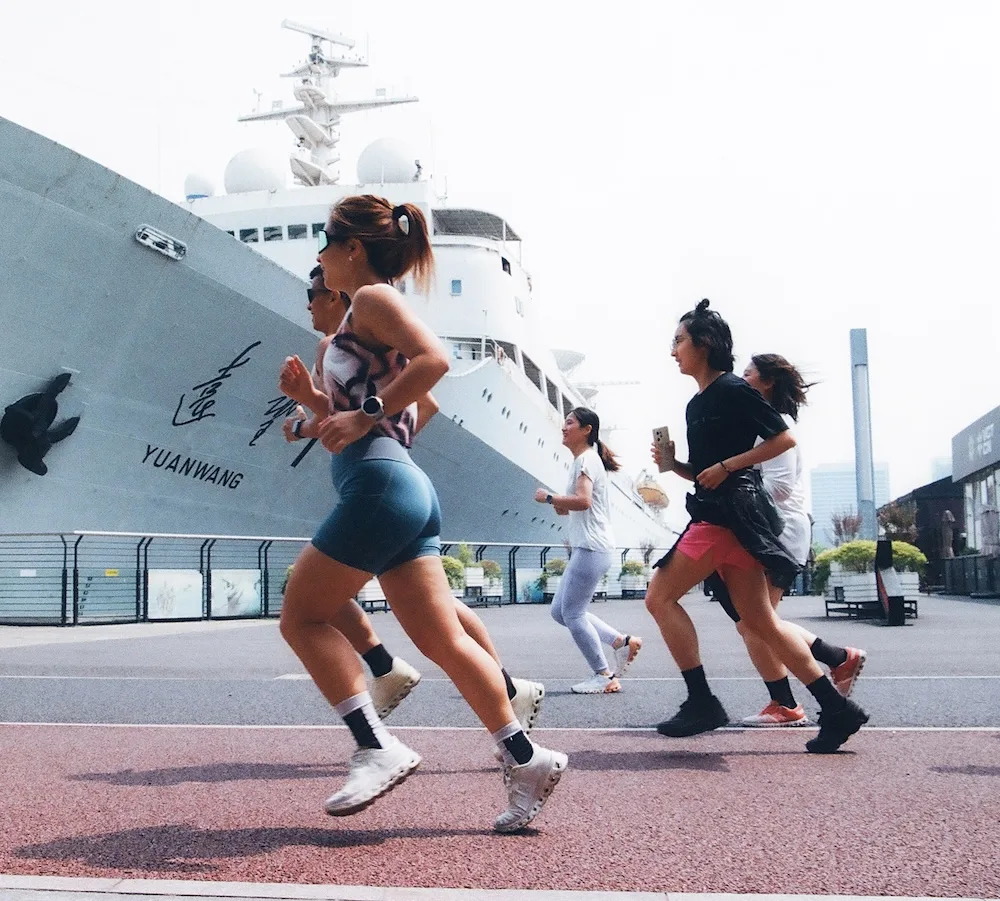 Several people jogging along a waterfront promenade past the large docked ship labeled "YUANWANG".