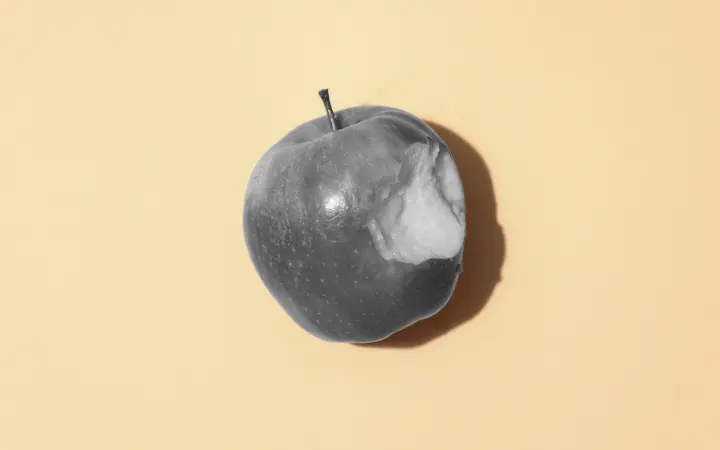 Black and white photo of an apple with a bite taken out against a yellow background.