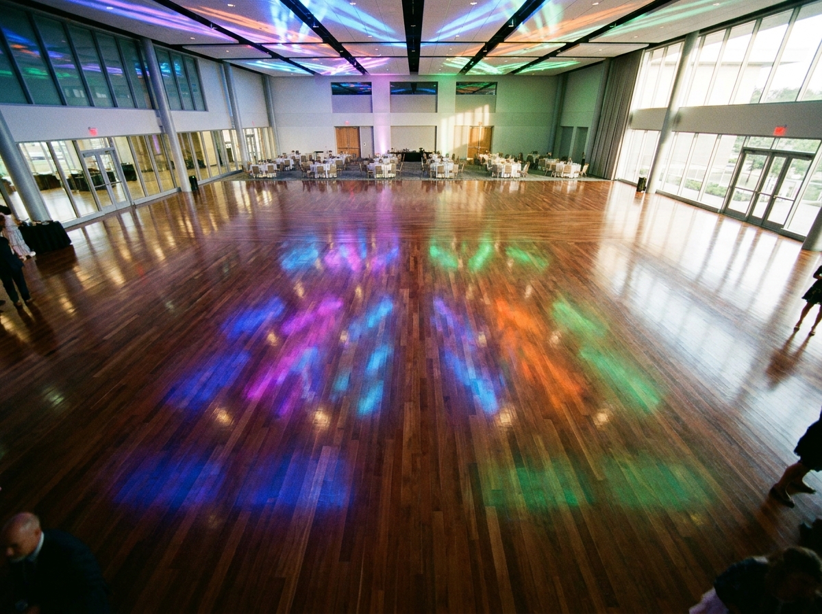 An empty, polished dance floor reflecting colorful lights, ready for a school dance event.