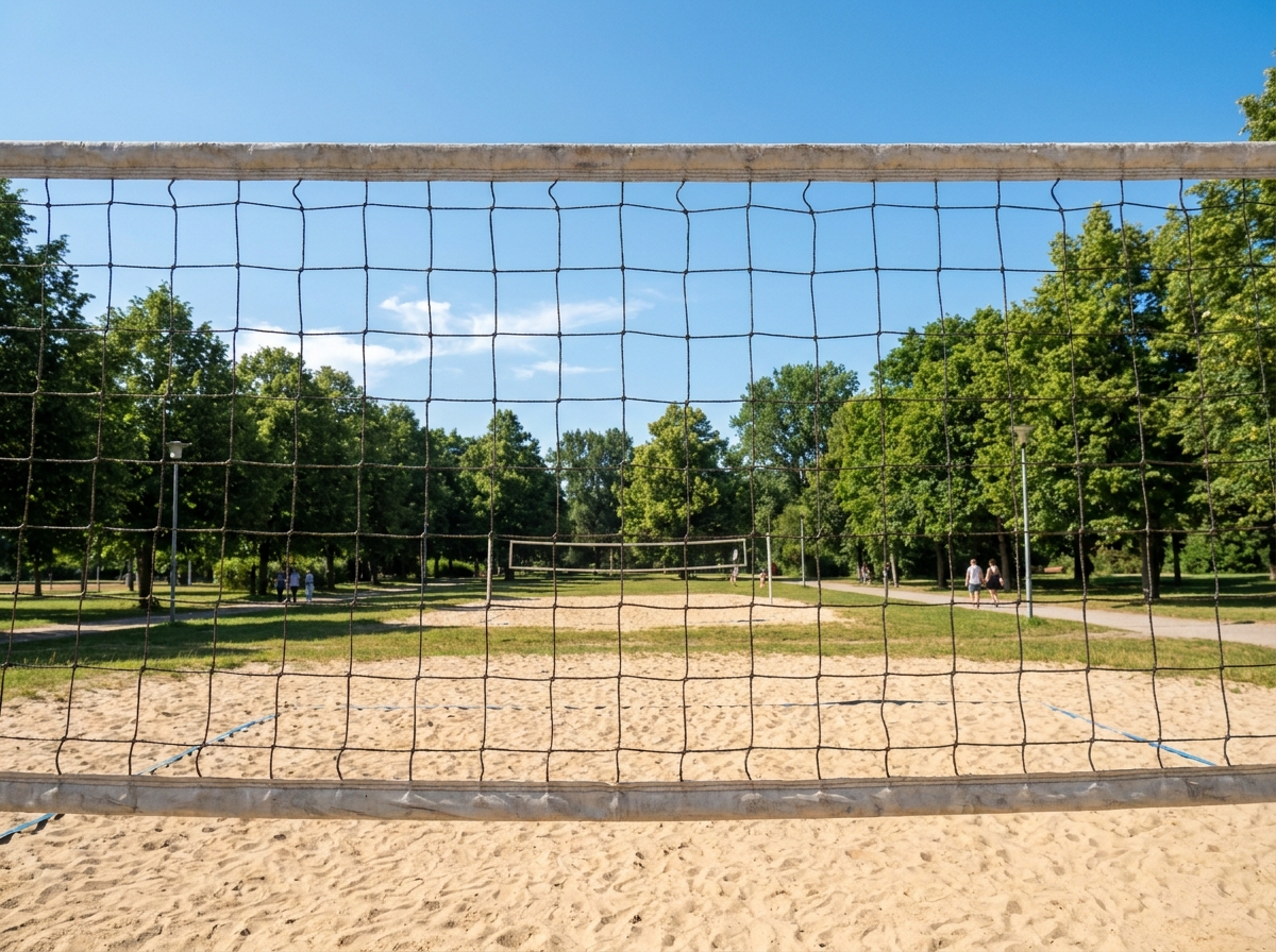 An empty outdoor volleyball court on a sunny day, seen through the net.