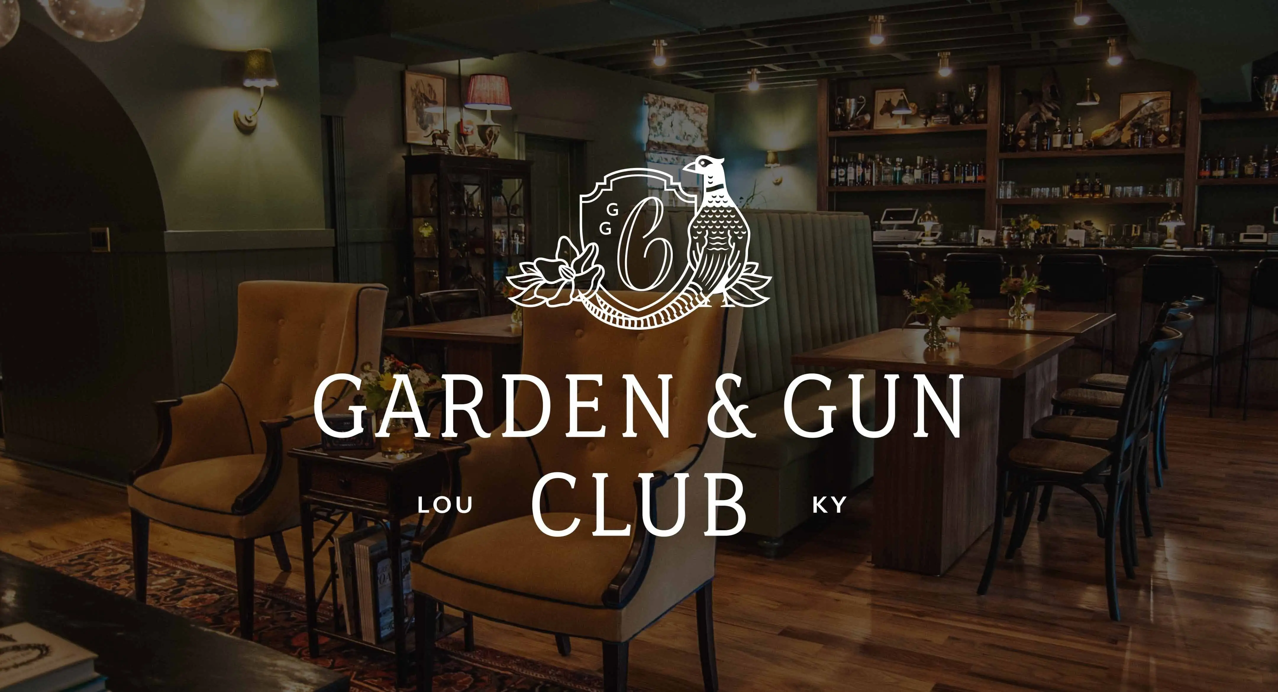 Interior of the Garden & Gun Club in Louisville, Kentucky. The image shows a cozy and elegant setting with plush armchairs, wooden tables, and a well-stocked bar in the background.
